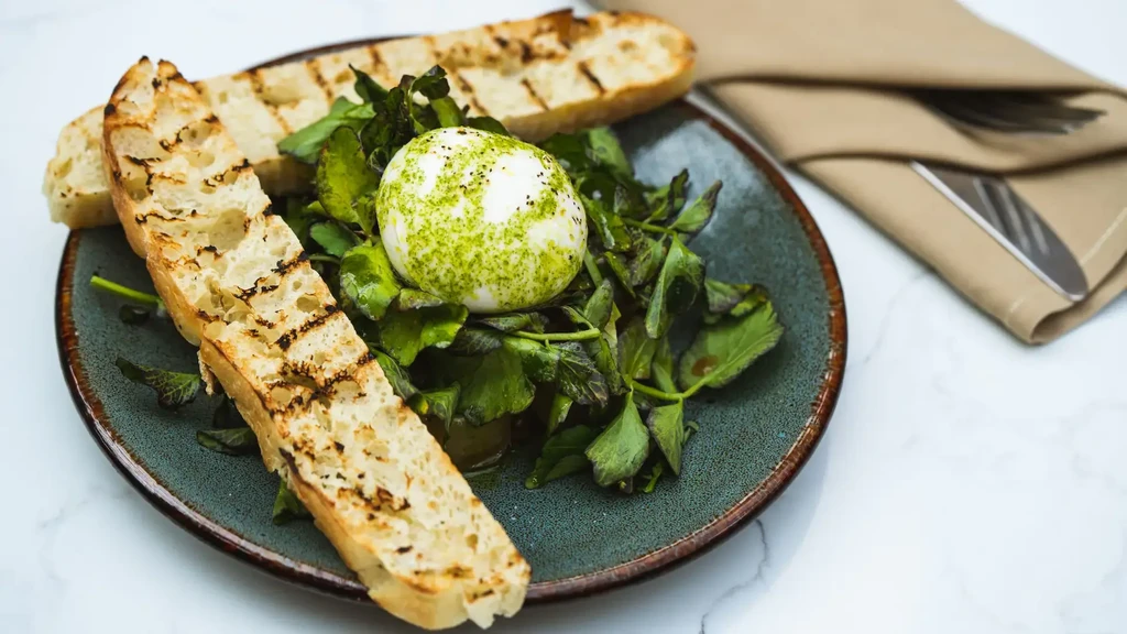 Grilled bread, burrata, and greens on a ceramic plate.