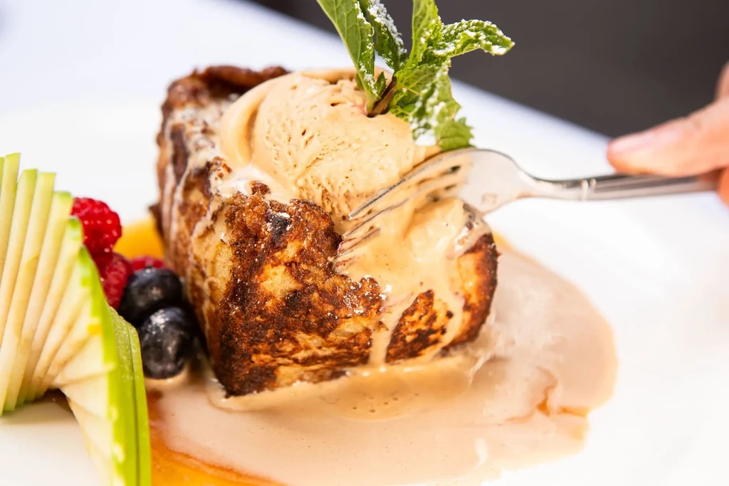 A fork piercing a piece of French toast with ice cream and fruit.