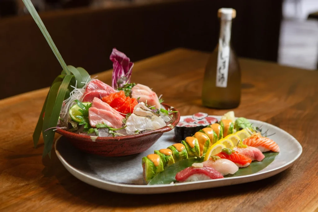 A platter of sushi and sashimi with a bottle of sake.