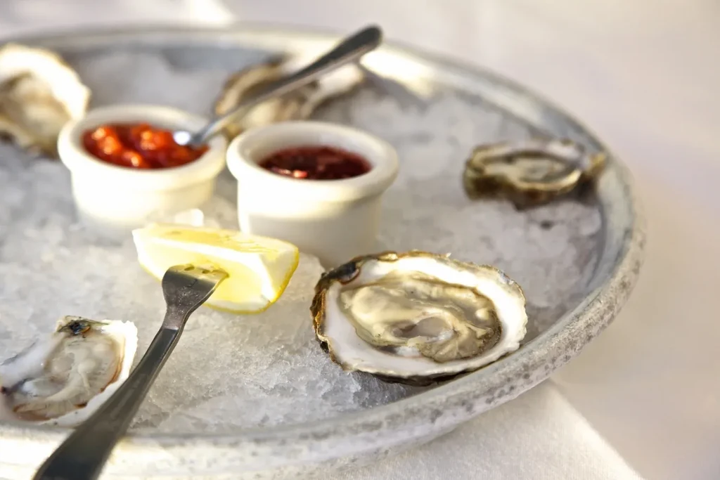 A plate of oysters on ice with sauces and a lemon wedge.