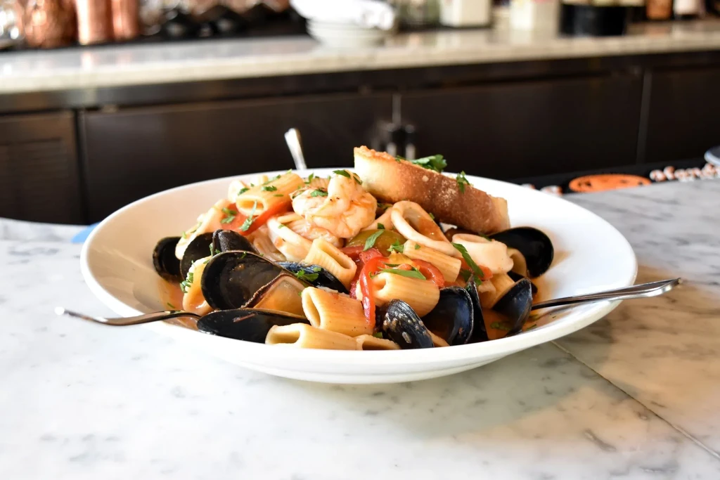 A white plate of seafood pasta with shrimp, mussels, and calamari.