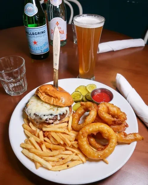 A cheeseburger with fries, onion rings, pickles, ketchup, and beer.