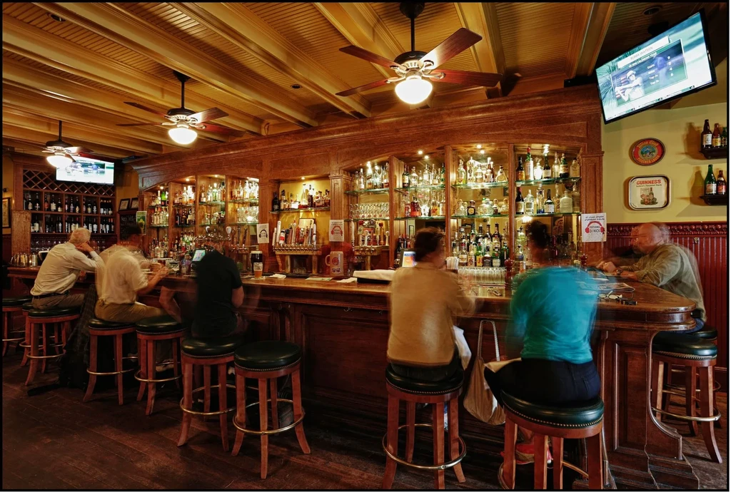 People sitting at a dark wooden bar with bottles on shelves.