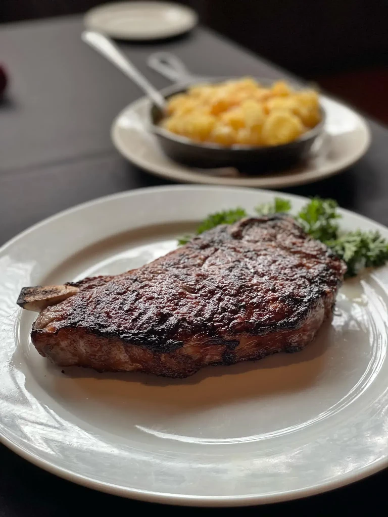 Grilled steak with parsley on a plate, macaroni and cheese blurred in background.