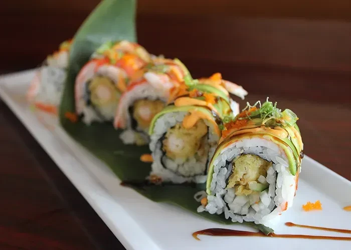 Elaborate sushi rolls with tempura, avocado, and tobiko on a plate.