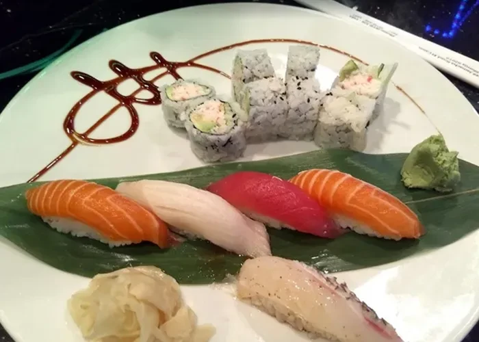 Assorted sushi and sashimi on a white plate with wasabi and ginger.