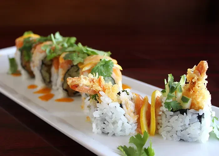 Sushi rolls with tempura shrimp, lemon, and cilantro on a white platter.