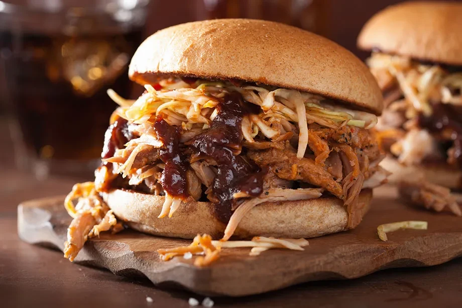 Saucy pulled pork sandwich with coleslaw on a rustic wooden board.
