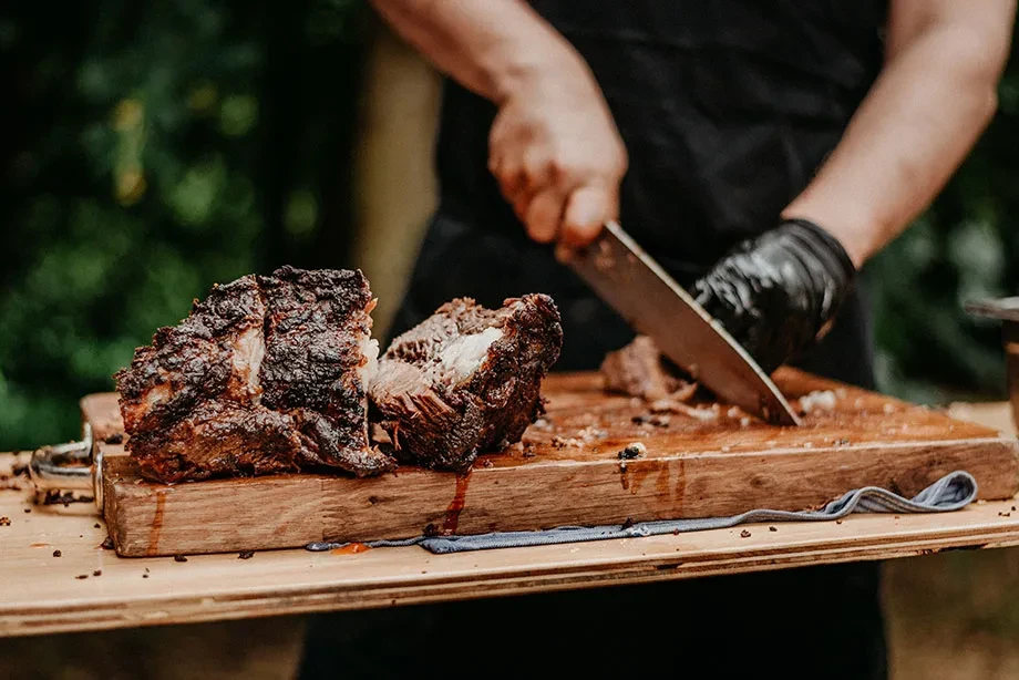 Gloved hands carving dark-crusted shredded meat on a wooden board.