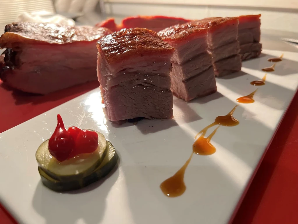 Crispy roasted pork belly, pickles, and sauces on a white plate.