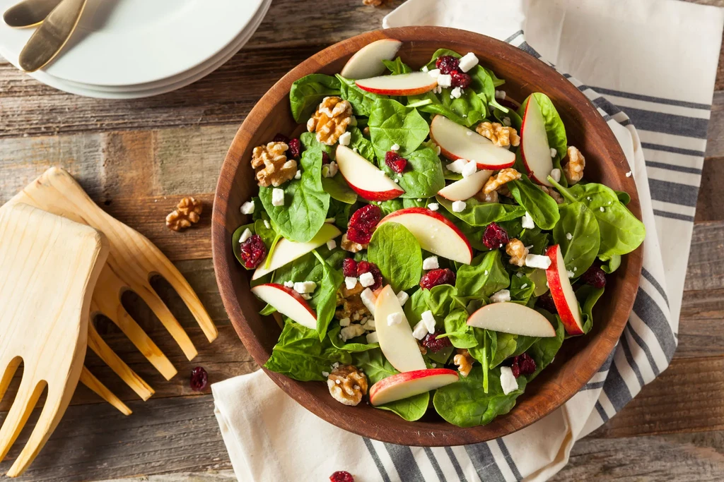 Spinach salad with apples, walnuts, cranberries, feta in wooden bowl.