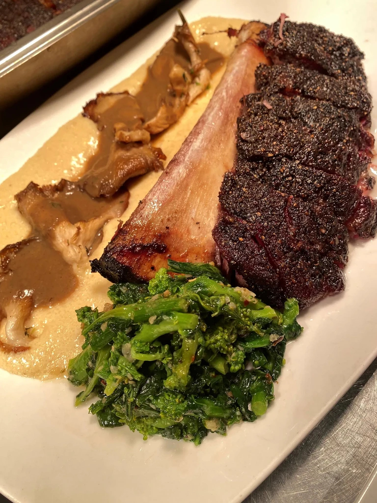 Braised short rib, polenta, mushrooms, and greens on a white plate.