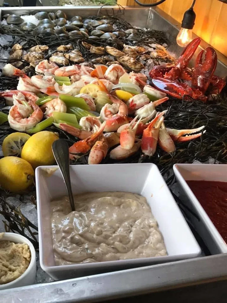 Abundant seafood display on ice with shrimp, lobster, crab, and sauces.