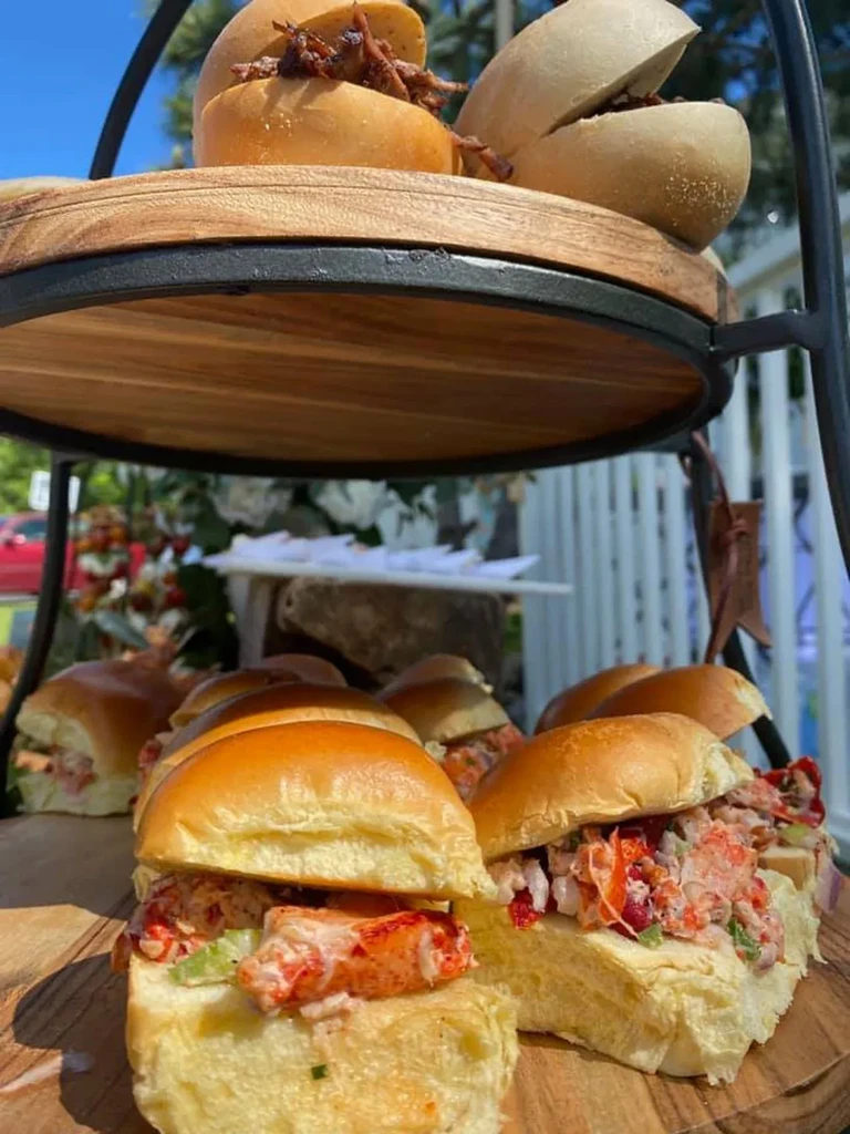 Tiered stand displaying lobster rolls and dark meat sliders outdoors.