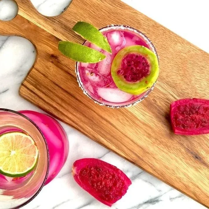Pink drinks with lime and prickly pear on a wooden board.