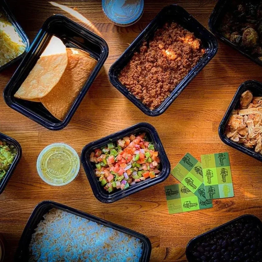 An overhead shot of various Mexican food items in black take-out containers.