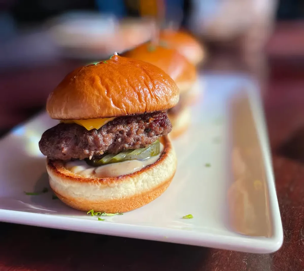 A delicious cheeseburger slider with pickles and sauce on a white plate.