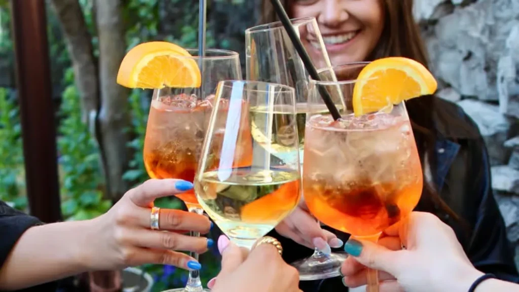 Four people clinking glasses of white wine and orange cocktails.