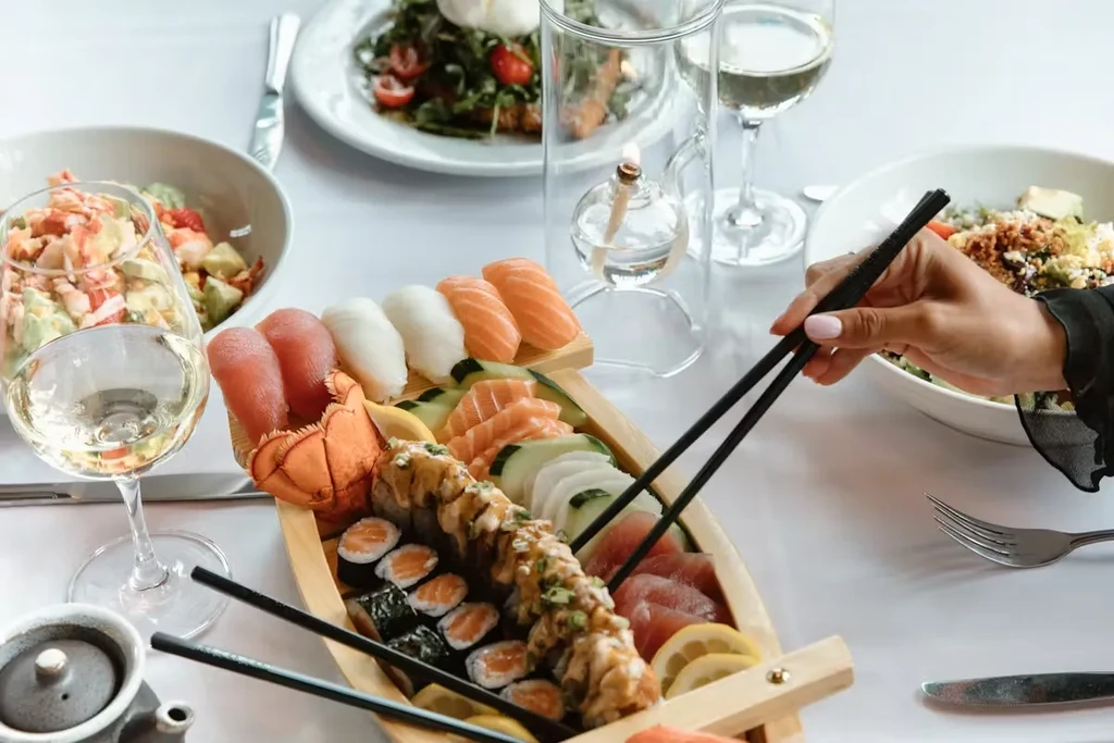 A person eating various sushi rolls and sashimi from a wooden boat.