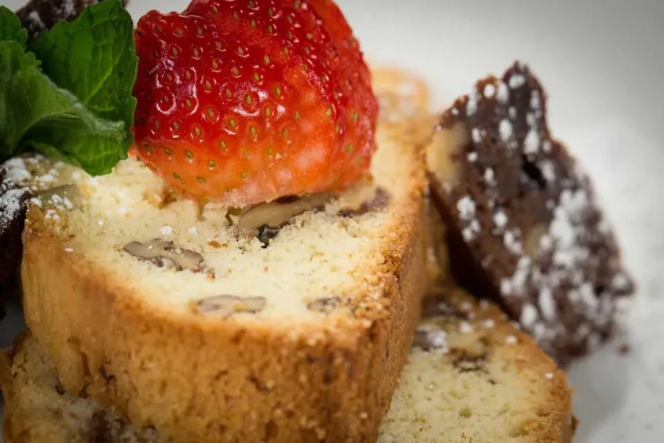 Slices of cake with nuts, strawberry, and powdered sugar on white plate.