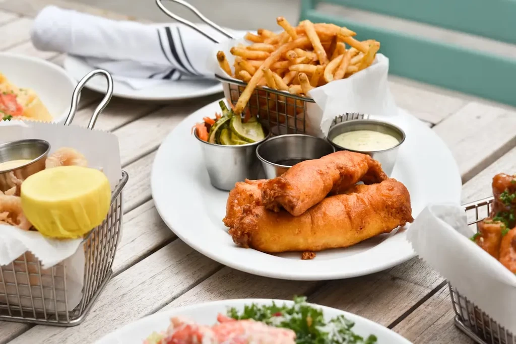 Fried fish and french fries with dipping sauces on a wooden table.