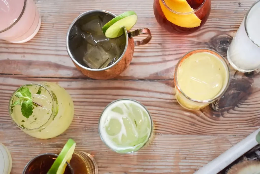 Overhead view of various colorful cocktails on a wooden table.