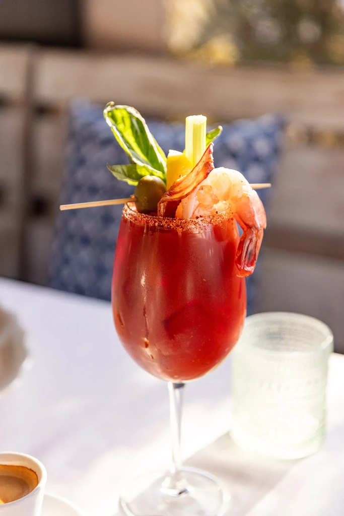 Bloody Mary cocktail in a goblet, garnished with shrimp, bacon, and celery.