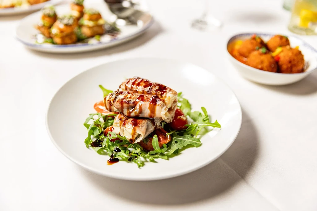 Three prosciutto-wrapped dishes with balsamic glaze on a bed of arugula and tomatoes.