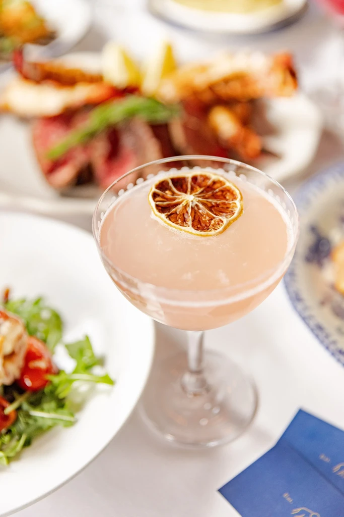 A light pink cocktail with a dried orange slice in a coupe glass.