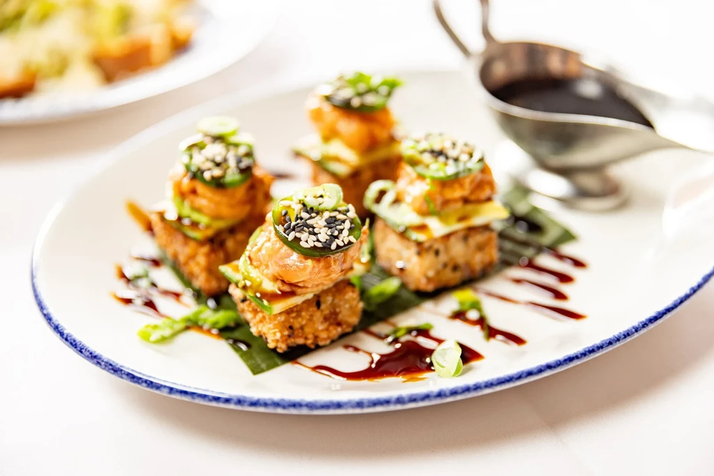 A plate of fried rice squares topped with fish, avocado, and jalapeños.