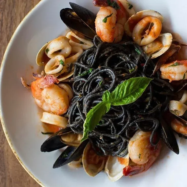A white plate of black squid ink pasta with seafood.