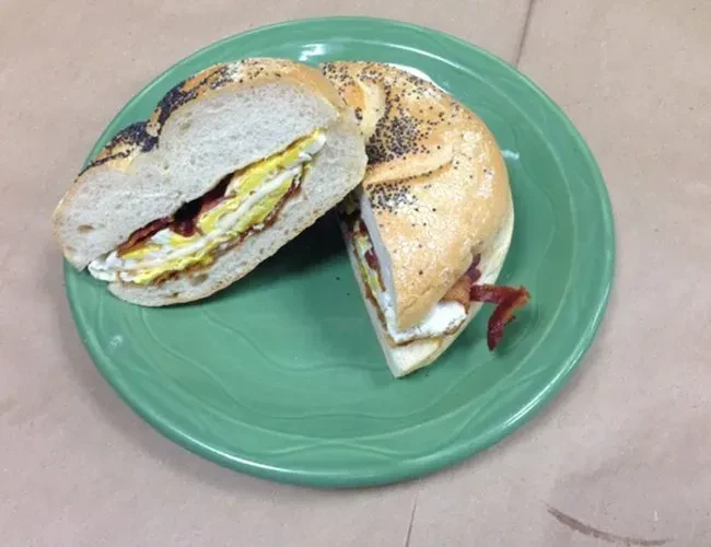 A poppy seed bagel sandwich with egg and bacon on a green plate.