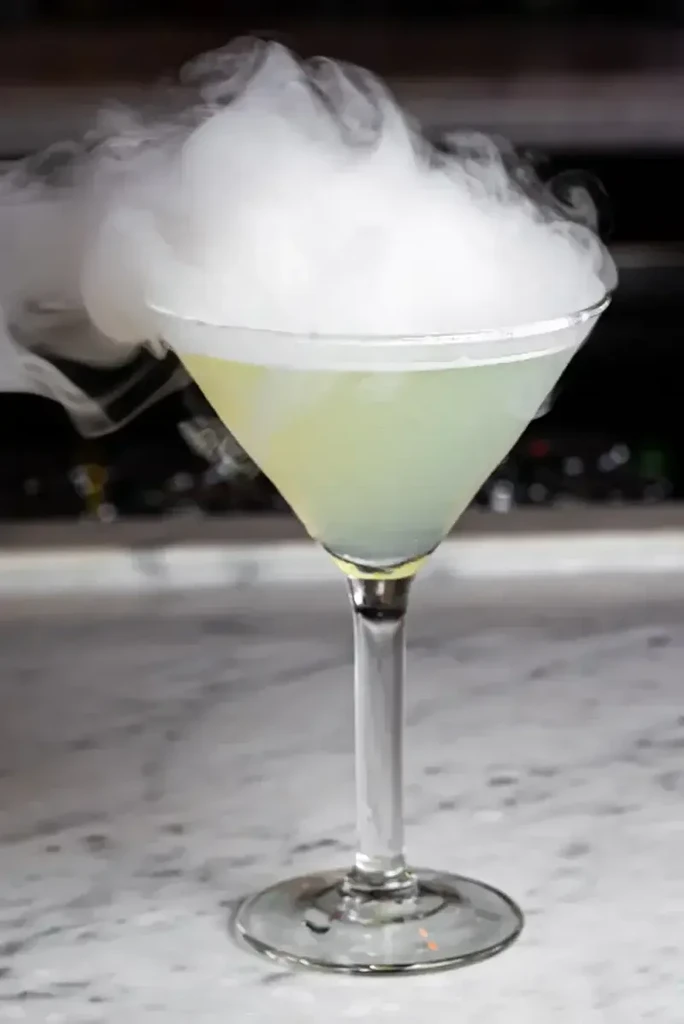 Martini glass with a smoking green cocktail on a marble surface.