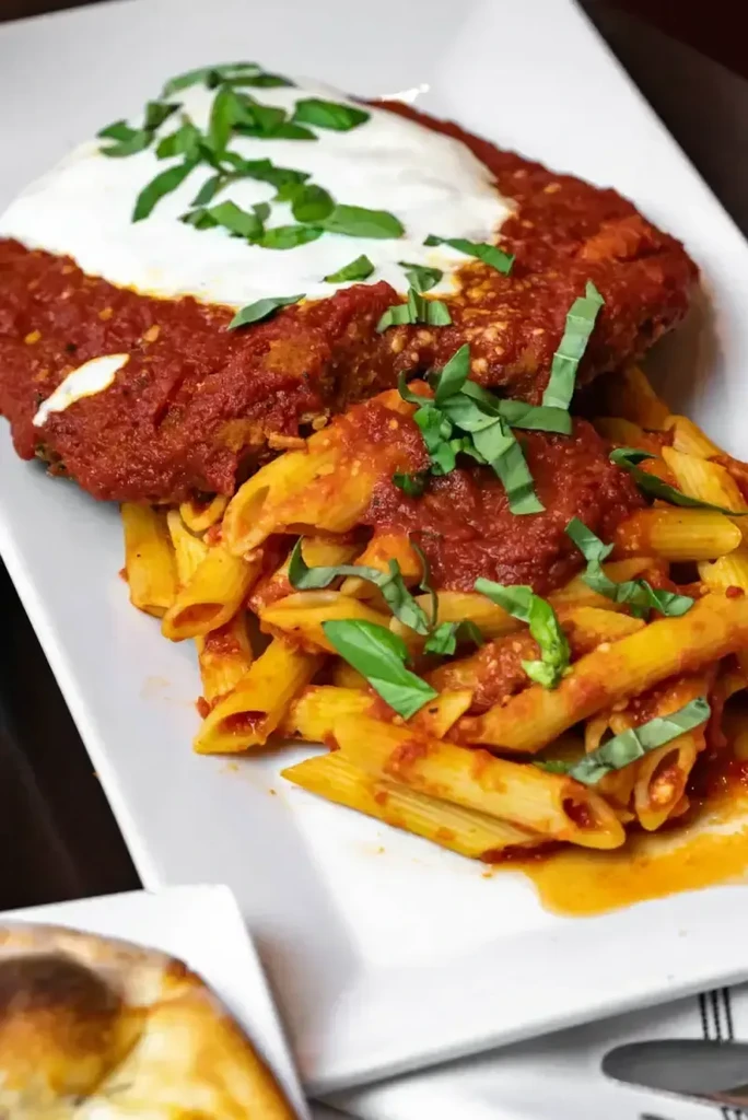 Chicken parmesan with penne pasta, tomato sauce, and basil.