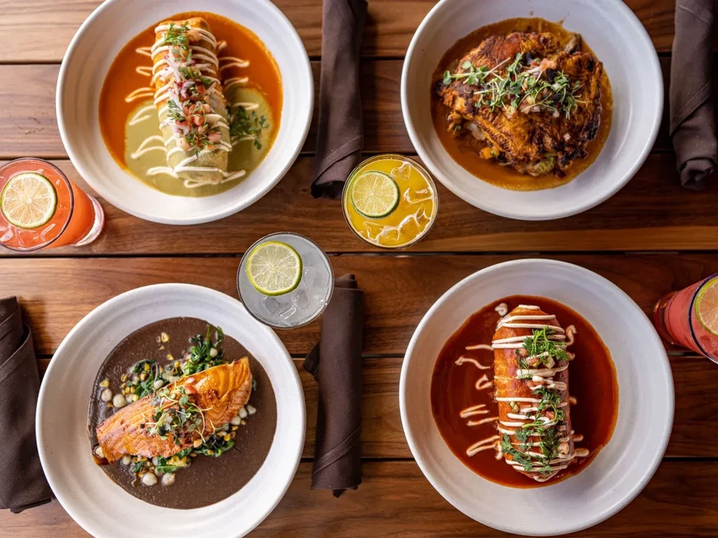 Four colorful meals and four cocktails on a wooden table.