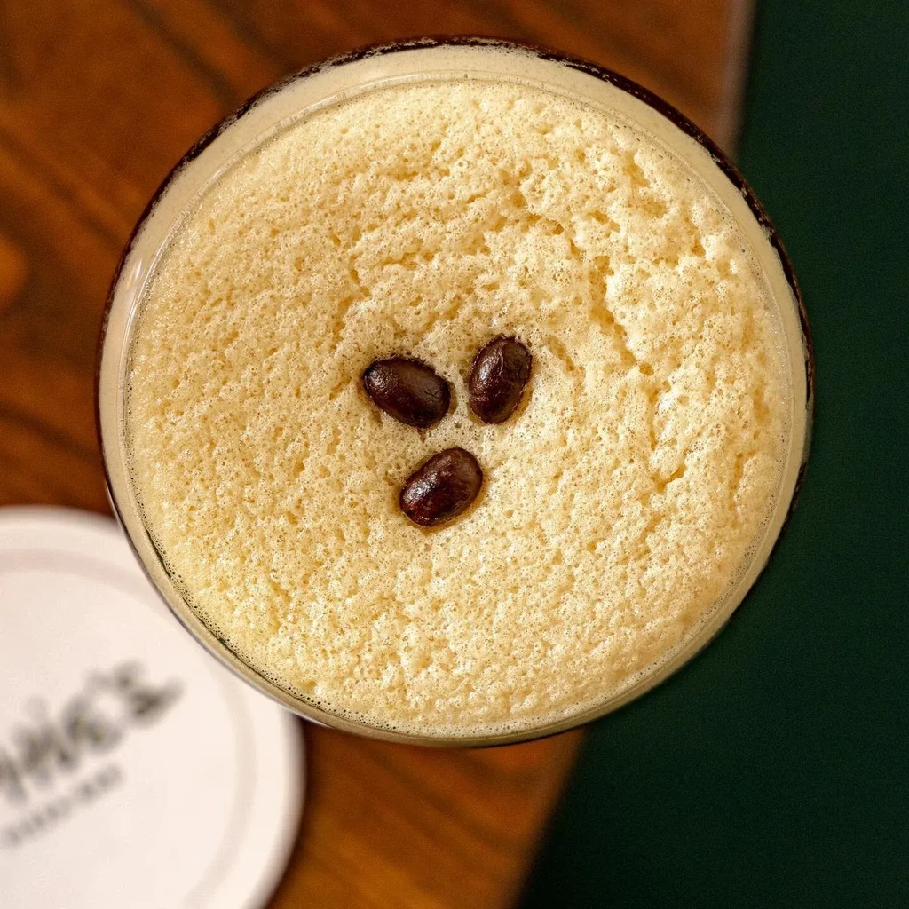 Overhead view of a foamy drink with three coffee beans on top.