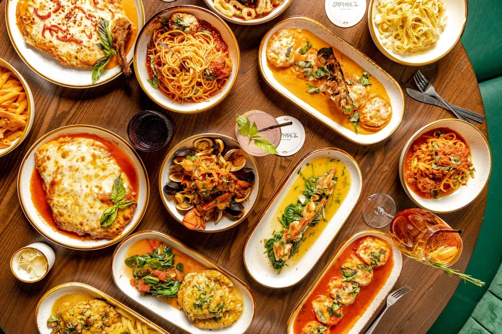 An overhead shot of a wooden table laden with various Italian dishes.