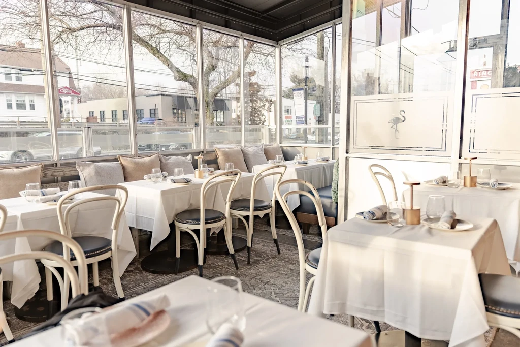 An empty, elegant restaurant dining room with white tablecloths and large windows.