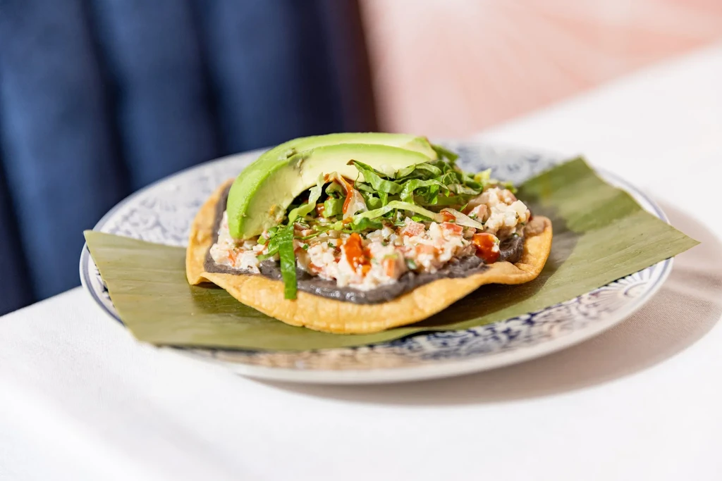 A tostada with black beans, ceviche, avocado, and lettuce on a banana leaf.