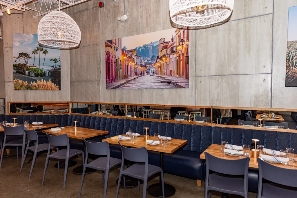 Modern restaurant interior with concrete walls, navy booths, and large travel photos.