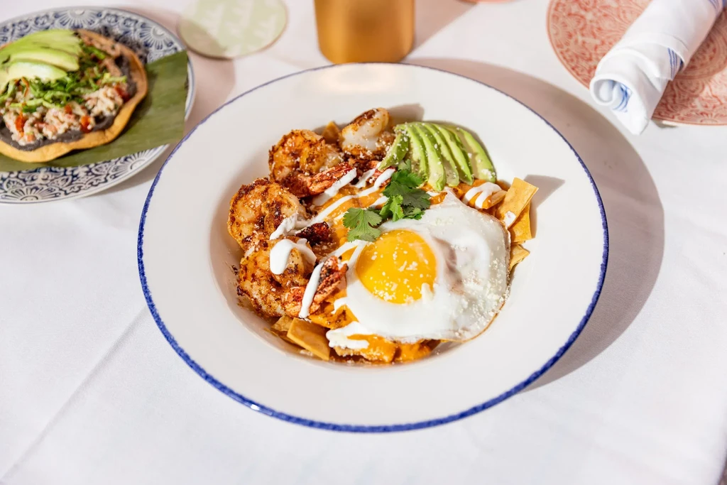 A dish with fried shrimp, avocado, fried egg, and tortilla chips.