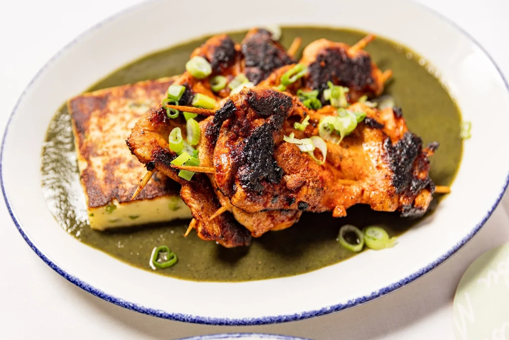 Grilled chicken skewers with green onion and a side of polenta in sauce.
