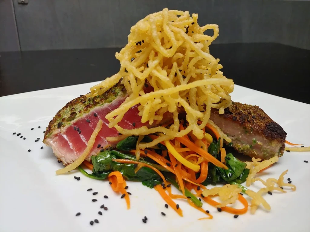 Seared tuna with crispy shoestring potatoes, carrots, spinach, and sesame seeds.