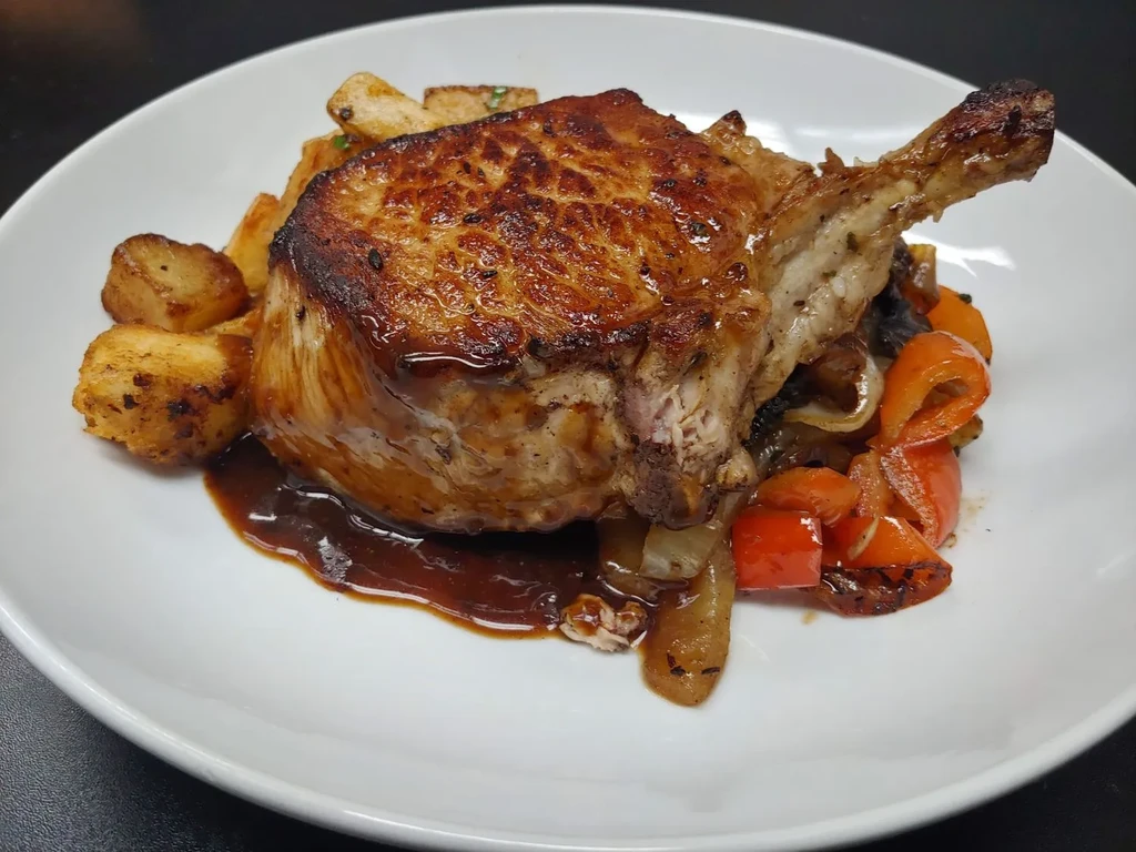 Seared pork chop with roasted potatoes, bell peppers, and onions.