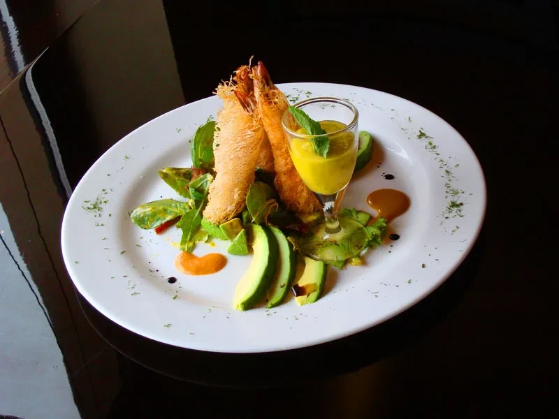 Fried shrimp with avocado, salad, and sauce on a white plate.