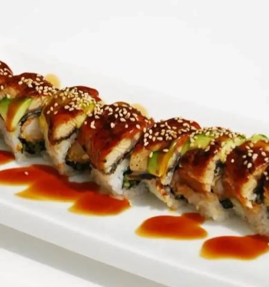 Sushi roll with eel, avocado, and sauce on a white plate.