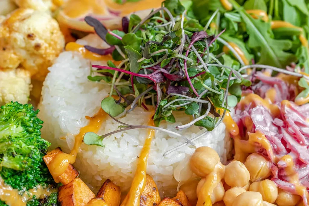 A colorful vegan bowl with rice, vegetables, chickpeas, and microgreens.