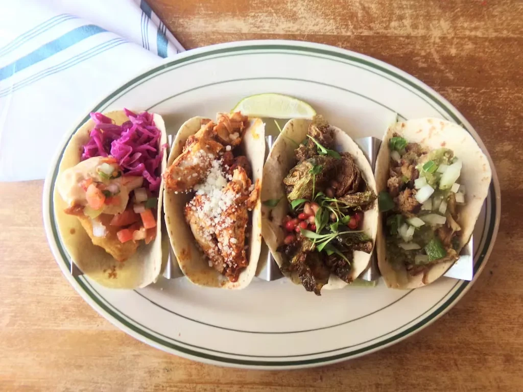 Four assorted tacos on a plate with a lime wedge.
