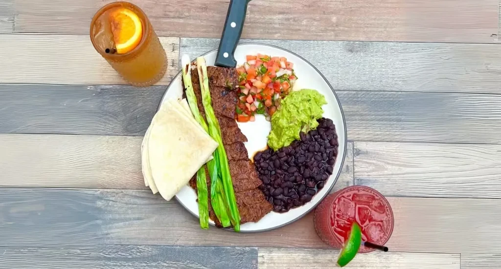 Overhead view of a fajita platter and two drinks on a wooden table.