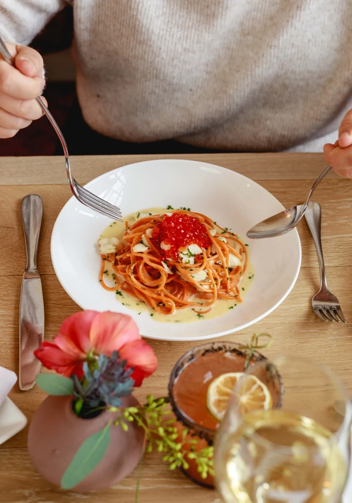 A person holding a fork and spoon, ready to eat spaghetti.
